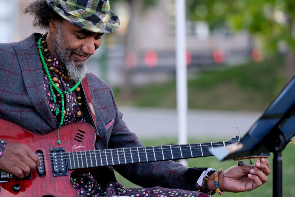 Waleed Abdulhamid smiling as he plays his guitar outdoors.